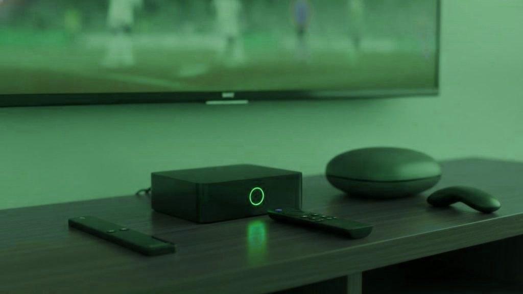 A streaming stick, a set-top box and a round streaming box with their remotes on a TV console