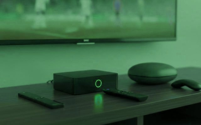 A streaming stick, a set-top box and a round streaming box with their remotes on a TV console