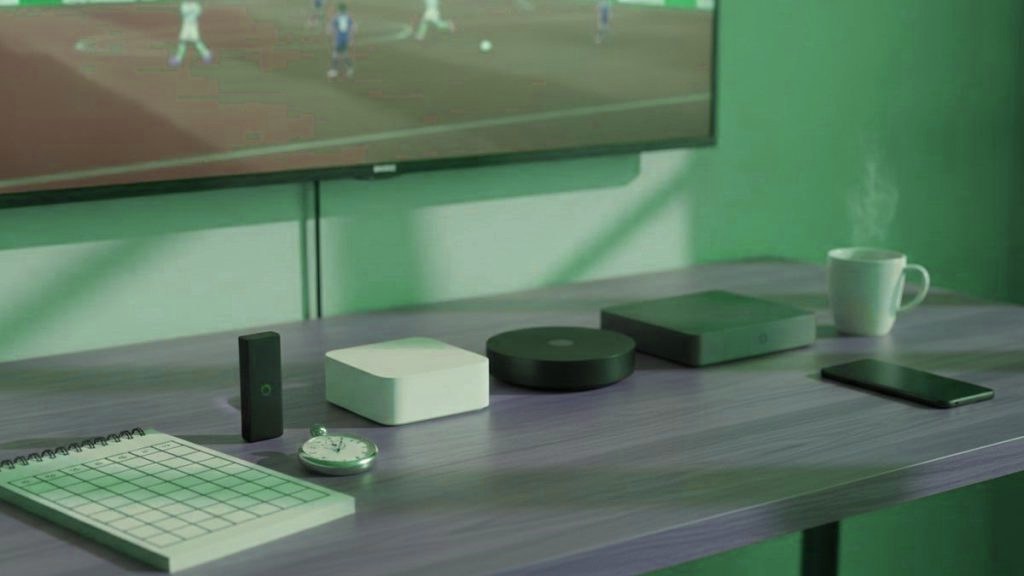 Five streaming devices, a notebook scoring grid and a stopwatch in front of a TV showing a football match